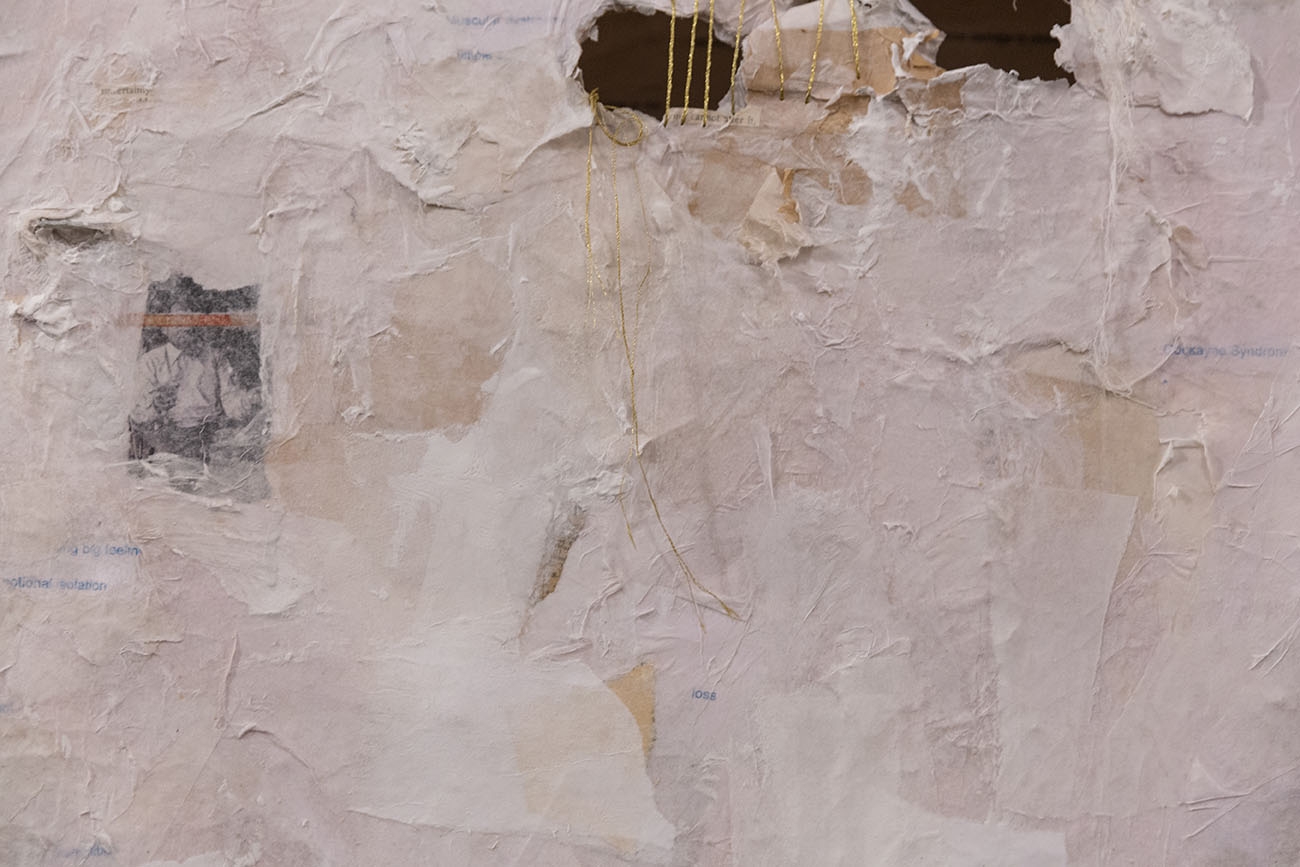 Image of a white canvas with swatches of white and off-white and one collaged photograph with an open portion sewn together