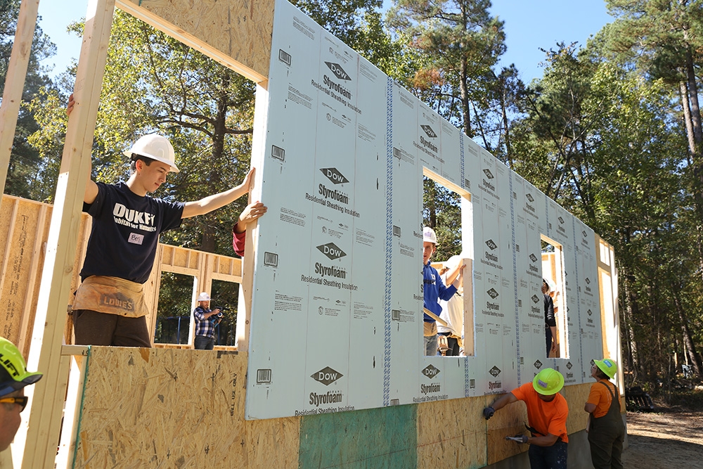 Duke students and community volunteers raise a wall on a Habitat for Humanity house
