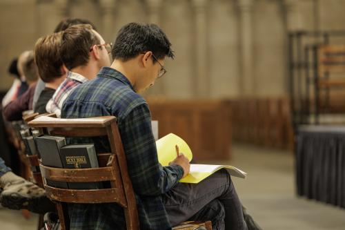 A man sitting in a chair writes on yellow paper.